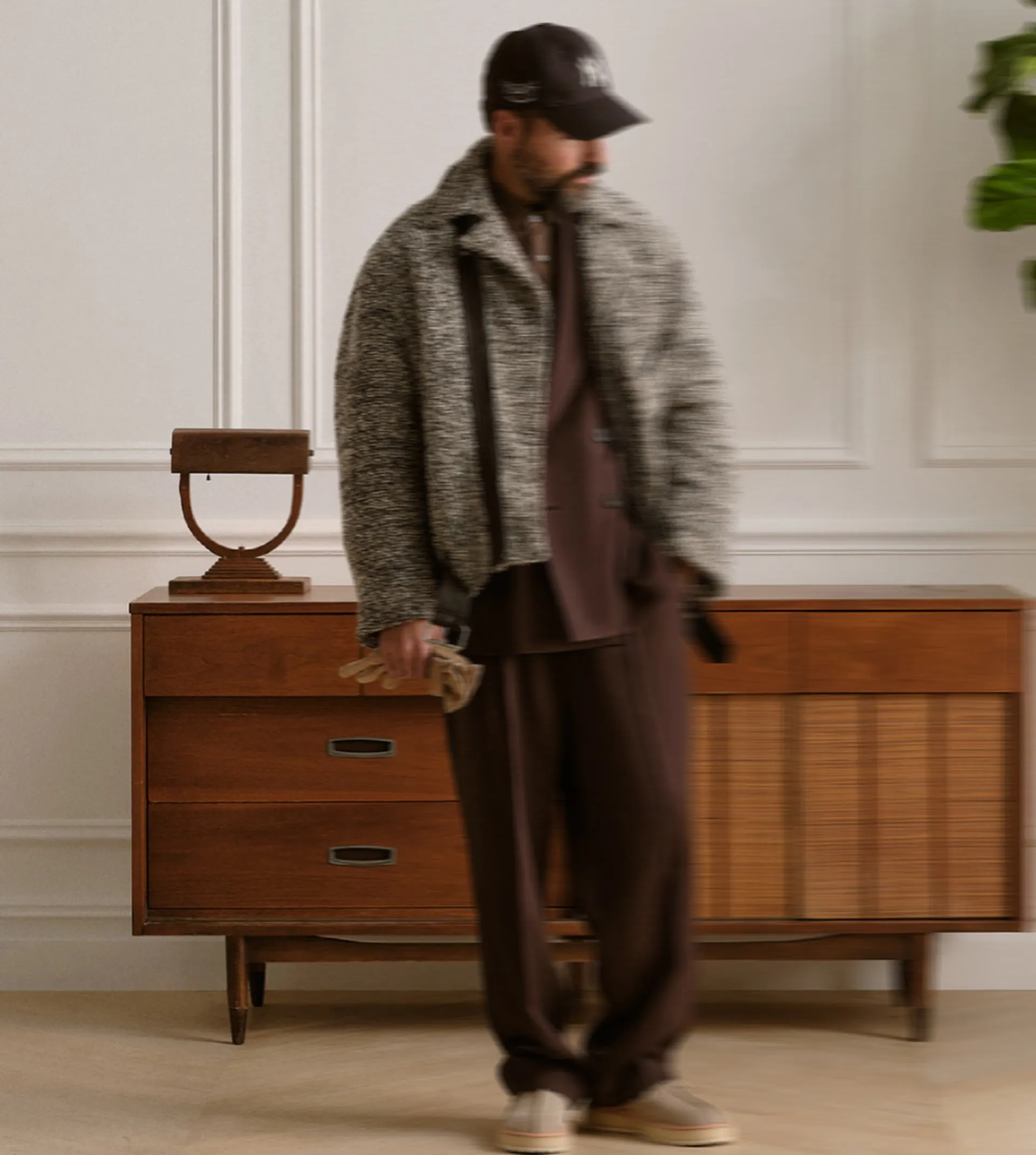 Man in a tweed jacket and cap standing beside a mid-century sideboard